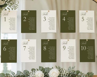 May include: A large arched mirror with a gold frame displayed on a wooden easel. The mirror features ten rectangular table seating cards numbered one through ten in alternating cream and olive green, decorated with white roses and greenery.