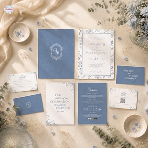 May include: A wedding stationery set featuring dusty blue and white cards with floral borders. The set includes an invitation for Anna Smith and Paul Laurent, RSVP cards, a details card, and envelopes, all displaying elegant serif typography and a monogram.