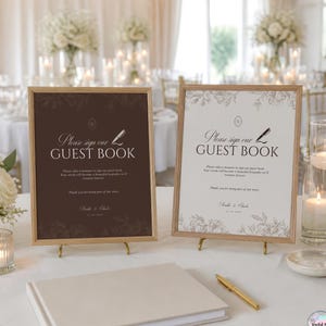 Puede incluir: Dos letreros enmarcados con marcos de madera clara, uno marrón oscuro y otro blanco, ambos con el texto 'Please sign our GUEST BOOK' con un icono de pluma, detalles de bordes florales y espacio para nombres y fecha, tras un libro de visitas.