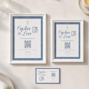 May include: Two white-framed signs and one matching rectangular card featuring the blue text Capture the Love, a smartphone and camera icon, a QR code, and the names Anna and Paul, designed to help guests share photos at a special event.