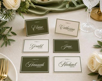 May include: Six rectangular folded place cards with a double-line border, alternating between olive green and cream backgrounds. Each card features the text TABLE followed by a number and a name in a script font, including Elaine Anderson, Catherine Jackson, Gerald Hanes, Jane Scott, Hannah Jones, and Michael Smith.