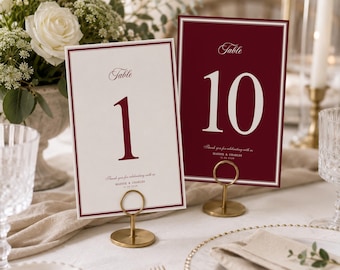 May include: Two rectangular table number cards held by gold circular stands. One card is cream with a burgundy border and the number 1, the other is burgundy with a white border and the number 10. Both feature the text Table, Thank you for celebrating with us, Maddie & Charles, and 10.26.2024.