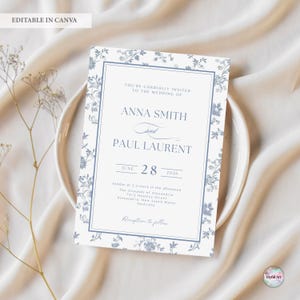 K&ouml;nnte beinhalten: Eine Hochzeitseinladung mit einem floralen Design in Blau- und Wei&szlig;t&ouml;nen. Die Einladung enth&auml;lt die Namen Anna Smith und Paul Laurent, das Datum 28. Juni 2026 und die Empfangsdetails. Der Text "EDITABLE IN CANVA" steht oben.
