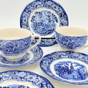 Può includere: Un set di stoviglie in porcellana blu e bianca, tra cui tazze da tè, piattini e piatti. I piatti e le tazze presentano un design paesaggistico dettagliato con bordi floreali. Il set include una varietà di forme e dimensioni.