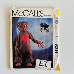 May include: Vintage McCall's sewing pattern featuring E.T. The Extra-Terrestrial. The pattern cover shows E.T. with a red heart and a silhouette of a bicycle with two riders against a blue background. The pattern number is 8311.