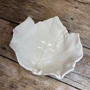 May include: White ceramic leaf-shaped dish. The dish is designed to look like a single leaf with a raised vein pattern.