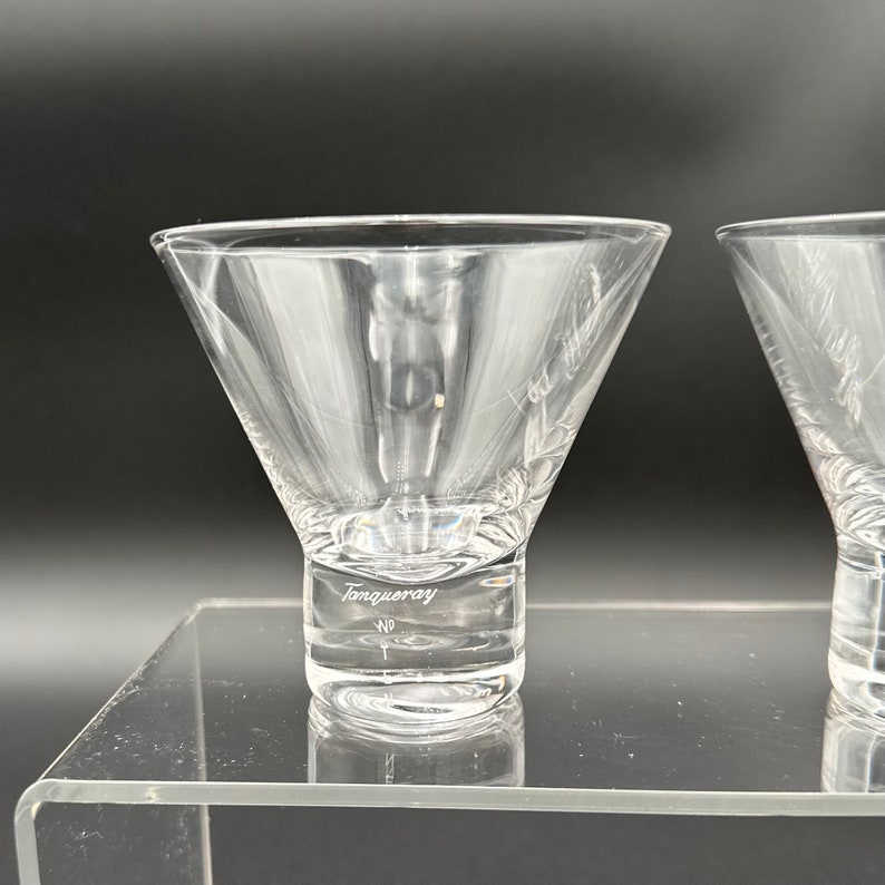 Peut inclure: Deux verres &agrave; martini en verre transparent avec un pied &eacute;pais. Le pied d'un verre porte l'inscription "Tanqueray" grav&eacute;e.