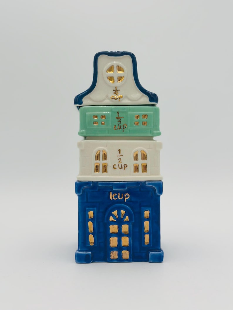 Vintage Anthropologie Sugar Cookie Townhouse Stacking Measuring Cups – Discontinued Holiday Kitchen Decor. A blue and white ceramic measuring cup set shaped like a house. The set includes four cups: 1 cup, 1/2 cup, 1/3 cup, and 1/4 cup.