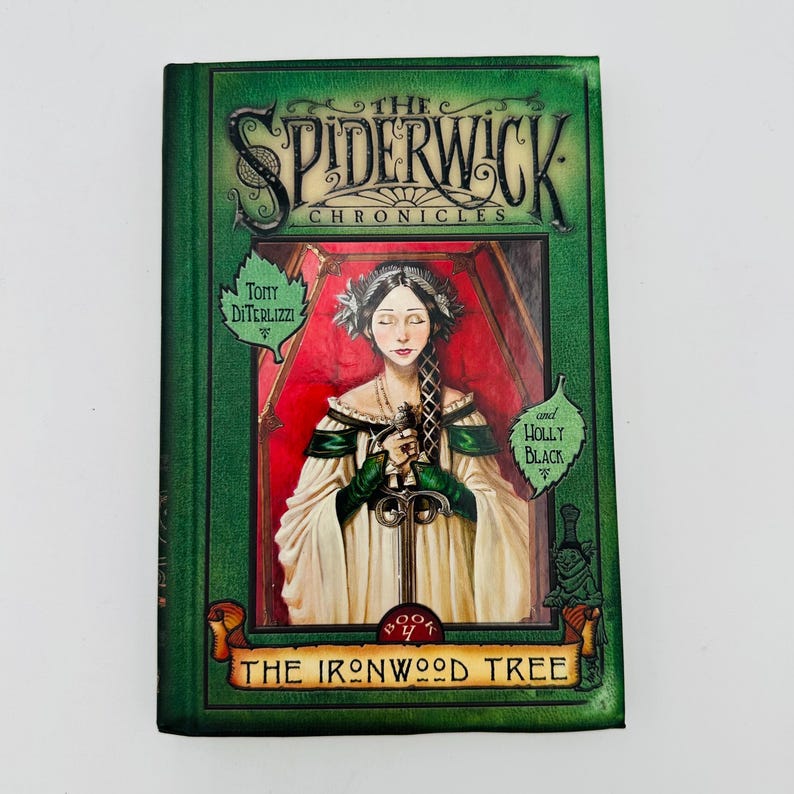 Puede incluir: Un libro de tapa dura titulado "The Spiderwick Chronicles: The Ironwood Tree". La portada presenta un retrato de una mujer sosteniendo una espada, sobre un fondo rojo. El libro tiene un borde verde con los nombres de los autores.