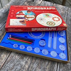 May include: A vintage Spirograph drawing set in a blue and brown box. The box has a red lid with the words "Kenner's Spirograph" and "New Spirograph" printed on it. The set includes a variety of plastic gears, rulers, and pens.
