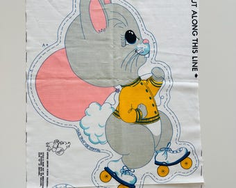 May include: A fabric panel featuring a cartoon bunny wearing a yellow jacket and roller skates. The bunny is gray with blue accents and a pink tail. Text on the panel reads "CUT ALONG THIS LINE" and "TEAR OPEN FOR STUFFING".