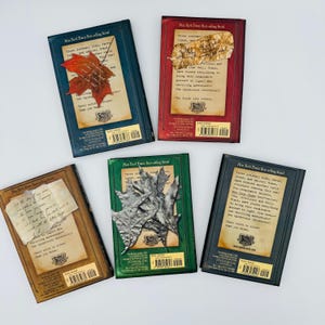 Puede incluir: Se muestran cinco libros con cubiertas de diferentes colores. Cada libro tiene un dise&ntilde;o &uacute;nico, que incluye una hoja roja, un trozo de pergamino y hojas plateadas. El texto en las cubiertas dice "New York Times Best-selling Serial."
