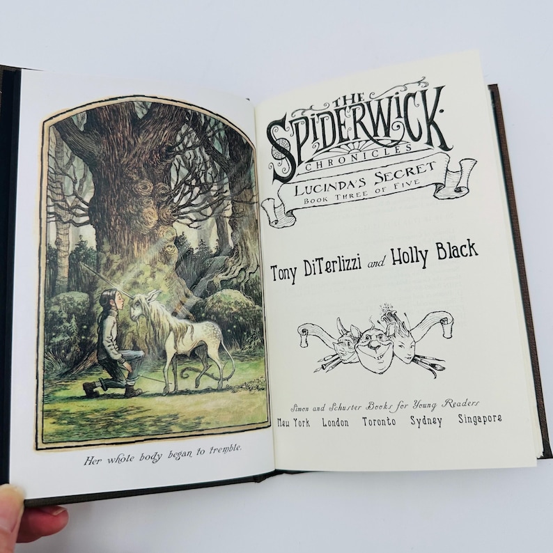 Puede incluir: Un libro abierto con ilustraciones y texto. La p&aacute;gina izquierda presenta un dibujo detallado de una persona arrodillada frente a un unicornio en un bosque. La p&aacute;gina derecha muestra el t&iacute;tulo "The Spiderwick Chronicles: Lucinda's Secret" y los nombres de los autores.