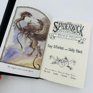 Puede incluir: Libro abierto con una cubierta negra. La ilustraci&oacute;n muestra un drag&oacute;n y un grifo. El texto dice "The Spiderwick Chronicles: The Wrath of Mulgarath, Book Five of Five" por Tony DiTerlizzi y Holly Black.
