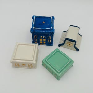 May include: Set of four miniature ceramic houses with gold accents. The houses are blue, white, green, and cream. The blue house has the text "Anthropologie" on the top.