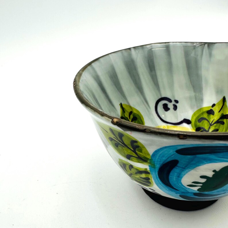Puede incluir: Un cuenco de cer&aacute;mica con un dise&ntilde;o floral pintado a mano. El cuenco presenta un patr&oacute;n floral azul y blanco con hojas verdes y una base negra. El interior tiene un patr&oacute;n de rayas en tonos grises y blancos.