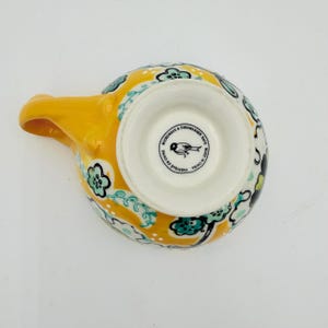 May include: Yellow ceramic spoon rest with a handle. The spoon rest has a floral pattern in teal, black, and white. The bottom of the spoon rest has the text "Microwave & Dishwasher Safe" and "Made in China".