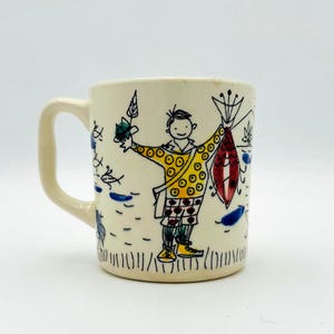 以下が含まれることがあります： 手描きのデザインが施された白いセラミックマグカップ。魚を持っている人が描かれています。その人は、赤と白のドット模様の黄色いシャツ、青いズボン、茶色の靴を履いています。魚は赤と白で、青いヒレが付いています。マグカップには青いハンドルが付いています。