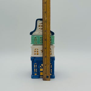 May include: A three-tiered ceramic house figurine with blue, white, and green paint. The house has gold accents and windows. The figurine is 7 inches tall.