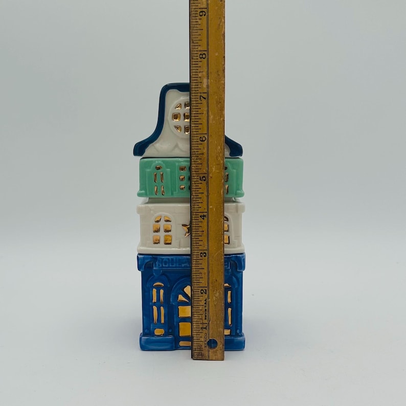May include: A three-tiered ceramic house figurine with blue, white, and green paint. The house has gold accents and windows. The figurine is 7 inches tall.
