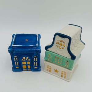 May include: Two ceramic houses with gold accents. The larger house is blue with white trim and the text "Anthropologie" on the top. The smaller house is white with blue trim and a green middle section. Both houses have gold stars on the front.