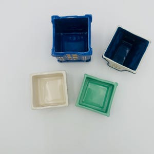 May include: Four ceramic square planters in different colors. The planters are empty and ready for plants. The planters are blue, white, green, and blue.
