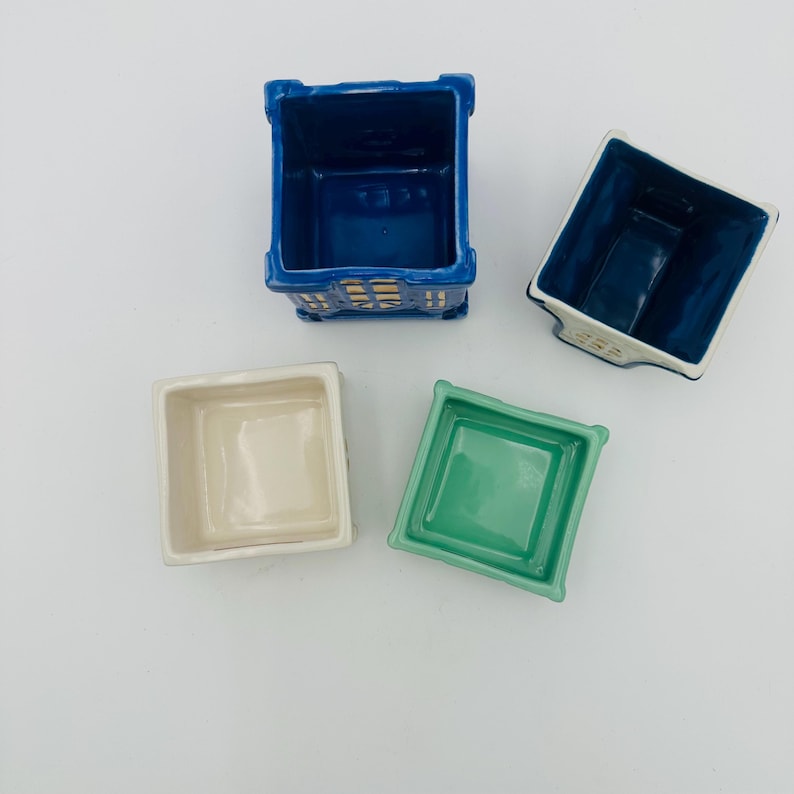 May include: Four ceramic square planters in different colors. The planters are empty and ready for plants. The planters are blue, white, green, and blue.