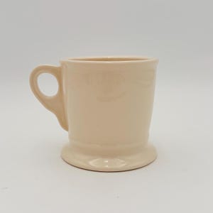 Puede incluir: Una taza de cer&aacute;mica de color crema con un asa redondeada y una base de pedestal. La taza tiene un acabado liso y brillante y un dise&ntilde;o simple y cl&aacute;sico. Esta taza es adecuada para caf&eacute;, t&eacute; u otras bebidas.
