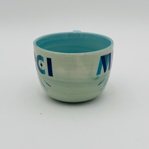 May include: A light blue ceramic mug with a white and blue geometric design. The mug has the words "Good Morning" written on it.