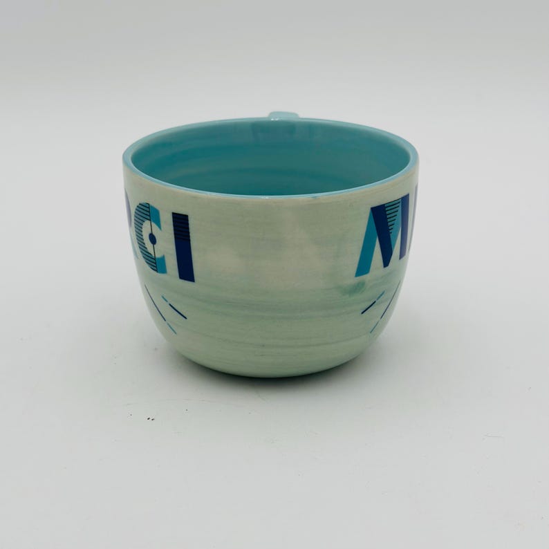 May include: A light blue ceramic mug with a white and blue geometric design. The mug has the words "Good Morning" written on it.