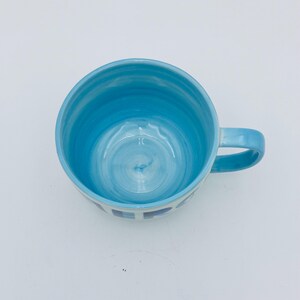 May include: A blue ceramic mug with a swirl design inside and a white stripe pattern around the bottom. The mug has a handle on the right side.