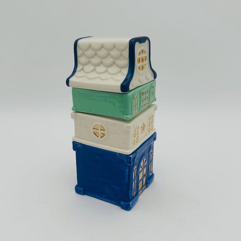 May include: A stack of four ceramic houses with blue, white, and green paint. The houses have gold accents and are stacked on top of each other.