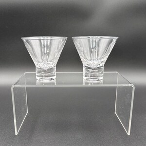 Peut inclure: Deux verres &agrave; martini en verre transparent sur un pr&eacute;sentoir en acrylique transparent. Les verres sont vides et ont une l&eacute;g&egrave;re l&egrave;vre autour du bord.