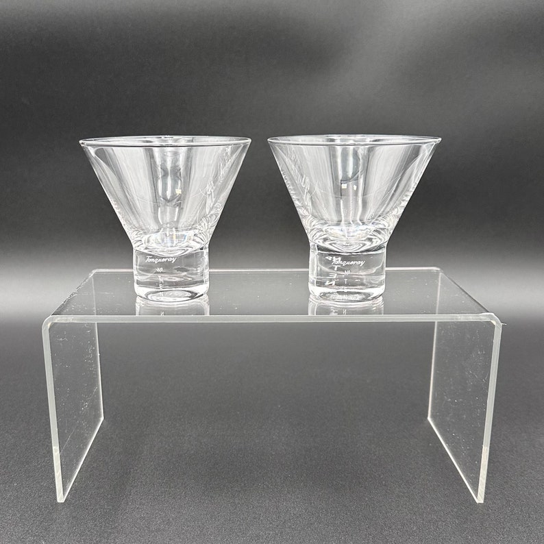 Peut inclure: Deux verres &agrave; martini en verre transparent sur un pr&eacute;sentoir en acrylique transparent. Les verres sont vides et ont une l&eacute;g&egrave;re l&egrave;vre autour du bord.