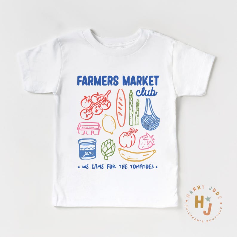 以下が含まれることがあります： カラフルなグラフィックデザインの白いTシャツ。デザインには「FARMERS MARKET club」の文字と「WE CAME FOR THE TOMATOES」のフレーズが含まれています。トマト、バゲット、イチゴなど、さまざまな果物や野菜のイラストも含まれています。