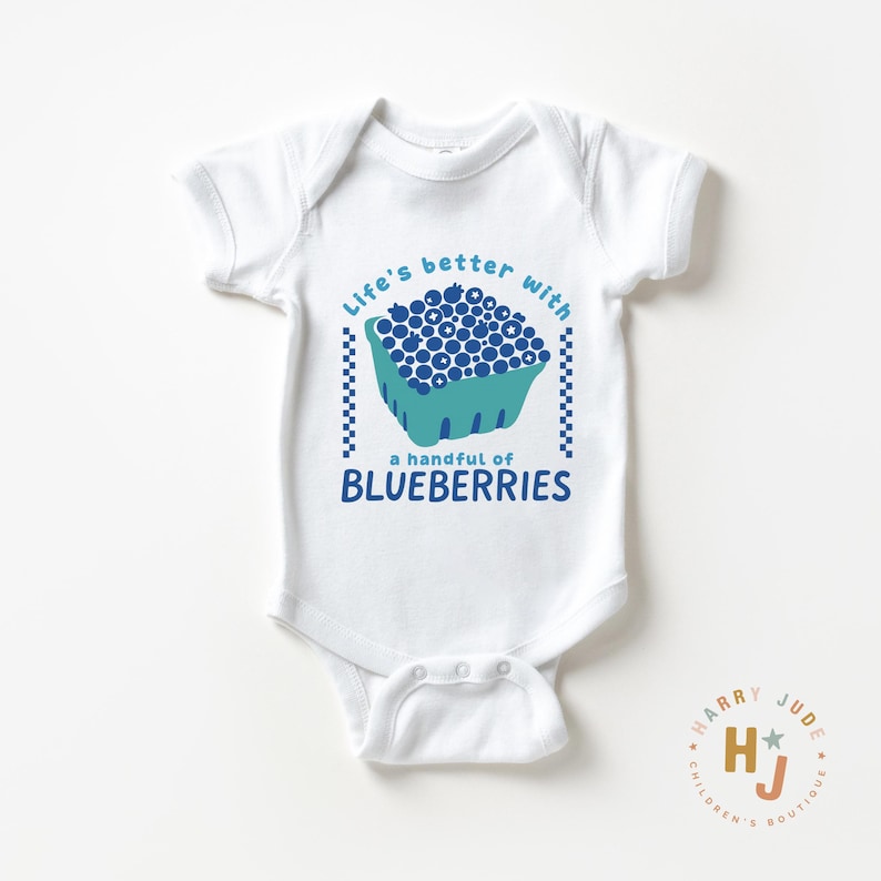May include: White baby onesie with a blue and teal graphic of blueberries in a basket. Text reads "Life's better with a handful of blueberries." The onesie has short sleeves and snap closures.