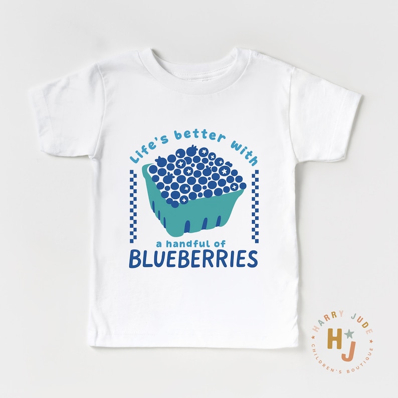 May include: White t-shirt with a blue and teal graphic. The graphic features a carton of blueberries and the text "Life's better with a handful of BLUEBERRIES". The shirt has short sleeves and a crew neck.