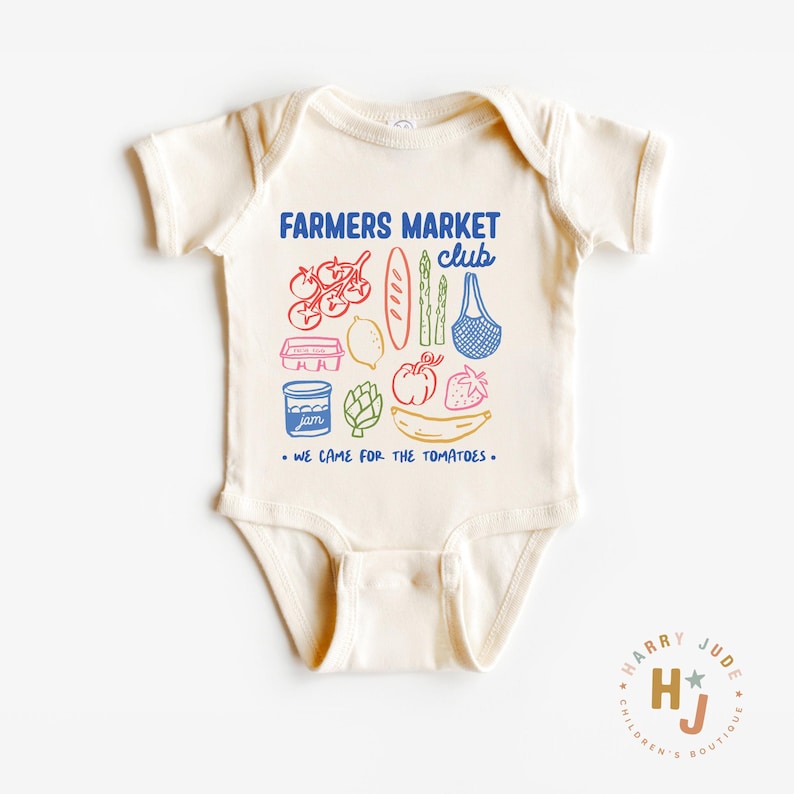 以下が含まれることがあります： クリーム色のベビーボディスーツ。カラフルなグラフィックが特徴です。「FARMERS MARKET club」と「WE CAME FOR THE TOMATOES」の文字が入っています。トマト、パン、アスパラガスなどのイラストも含まれています。