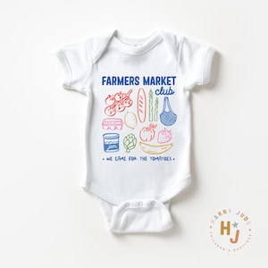 以下が含まれることがあります： カラフルな農産物のイラストと「FARMERS MARKET club」と「WE CAME FOR THE TOMATOES」の文字が入った白いベビーボディスーツ。デザインにはトマト、パン、アスパラガス、バナナが含まれています。