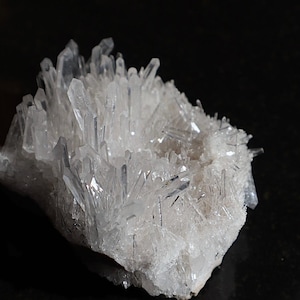 Può includere: Un gruppo di cristalli di quarzo trasparenti con una texture ruvida e naturale. I cristalli sono disposti in un motivo casuale e organico, creando una mostra unica e bellissima.