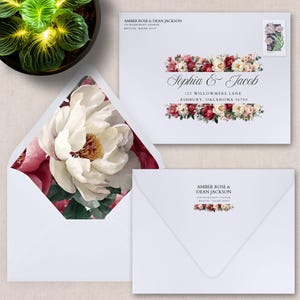 Könnte beinhalten: Weiße Hochzeitsumschläge mit floralen Akzenten. Ein Umschlag ist geöffnet und zeigt einen großen Pfingstrosen-Druck. Die anderen Umschläge tragen Namen und Adressen mit Blumenarrangements. Die Umschläge sind für eine Hochzeit.