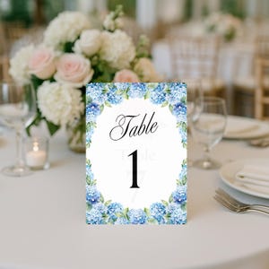 Pode incluir: Cartão de número de mesa floral azul e verde com o texto "Mesa 1" em preto.