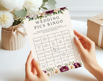 May include: A Wedding Pics Bingo game card with a floral border in cream, burgundy, and white. The card features a grid of squares with prompts like "Take a Wedding Selfie" and "Photo of the Best Man."