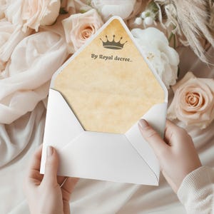 Può includere: Una busta bianca con un interno strutturato, simile alla pergamena. L'interno della busta presenta una grafica a corona e il testo "By Royal decree...". La busta è tenuta aperta, rivelando l'interno.