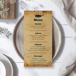 May include: A vintage-style menu card with a blue crown graphic at the top. The menu lists starters, entrees, desserts, and beverages. The card is on a wooden plate, with a white cloth and a white plate in the background.