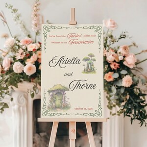Puede incluir: Un letrero de bienvenida de boda sobre un caballete de madera. El letrero crema dice "You've found the faeries' hidden door. Welcome to our Forevermore" y los nombres "Ariella and Thorne". Incluye ilustraciones de setas y una puerta de hadas.