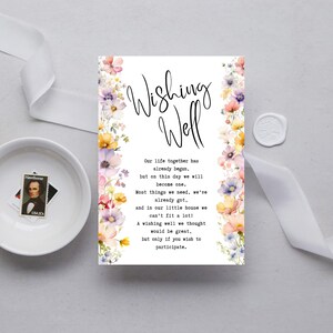 Może przedstawiać: Biała karta z napisem "Wishing Well" w eleganckiej czcionce, otoczona akwarelowymi ilustracjami kwiatowymi w odcieniach różu, żółci i fioletu. Karta zawiera tekst o wspólnym życiu pary.
