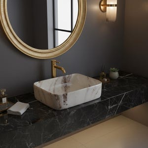 May include: A modern bathroom vanity with a rectangular marble sink. The sink is set on a black marble countertop. A gold-toned faucet and a round gold mirror are mounted on the dark gray wall. A small succulent and a candle are on the countertop.