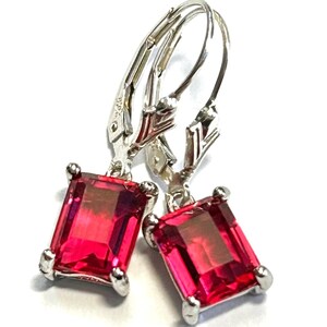 May include: A pair of leverback earrings featuring rectangular, vibrant red gemstones set in a silver-toned metal. The gemstones are faceted, catching the light and displaying a gradient of color. The earrings are displayed against a white background.