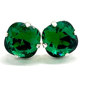 May include: A pair of stud earrings featuring large, faceted, emerald-green gemstones. The gems are round and set in a silver-colored metal. The earrings are displayed against a white background, highlighting their vibrant color and sparkle.